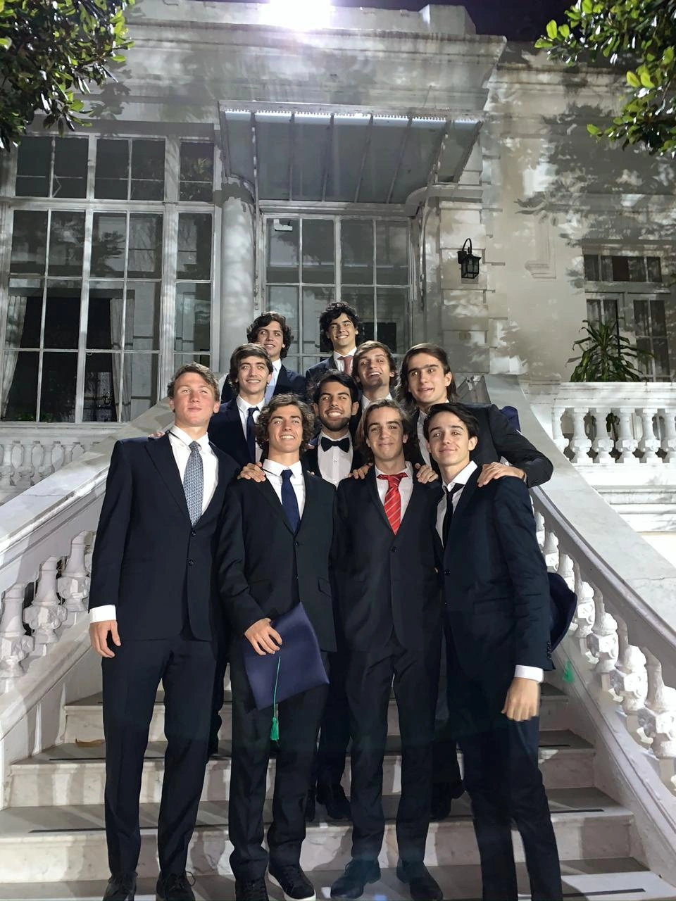 Facundo and friends in suits on the school steps, graduation cap in hand