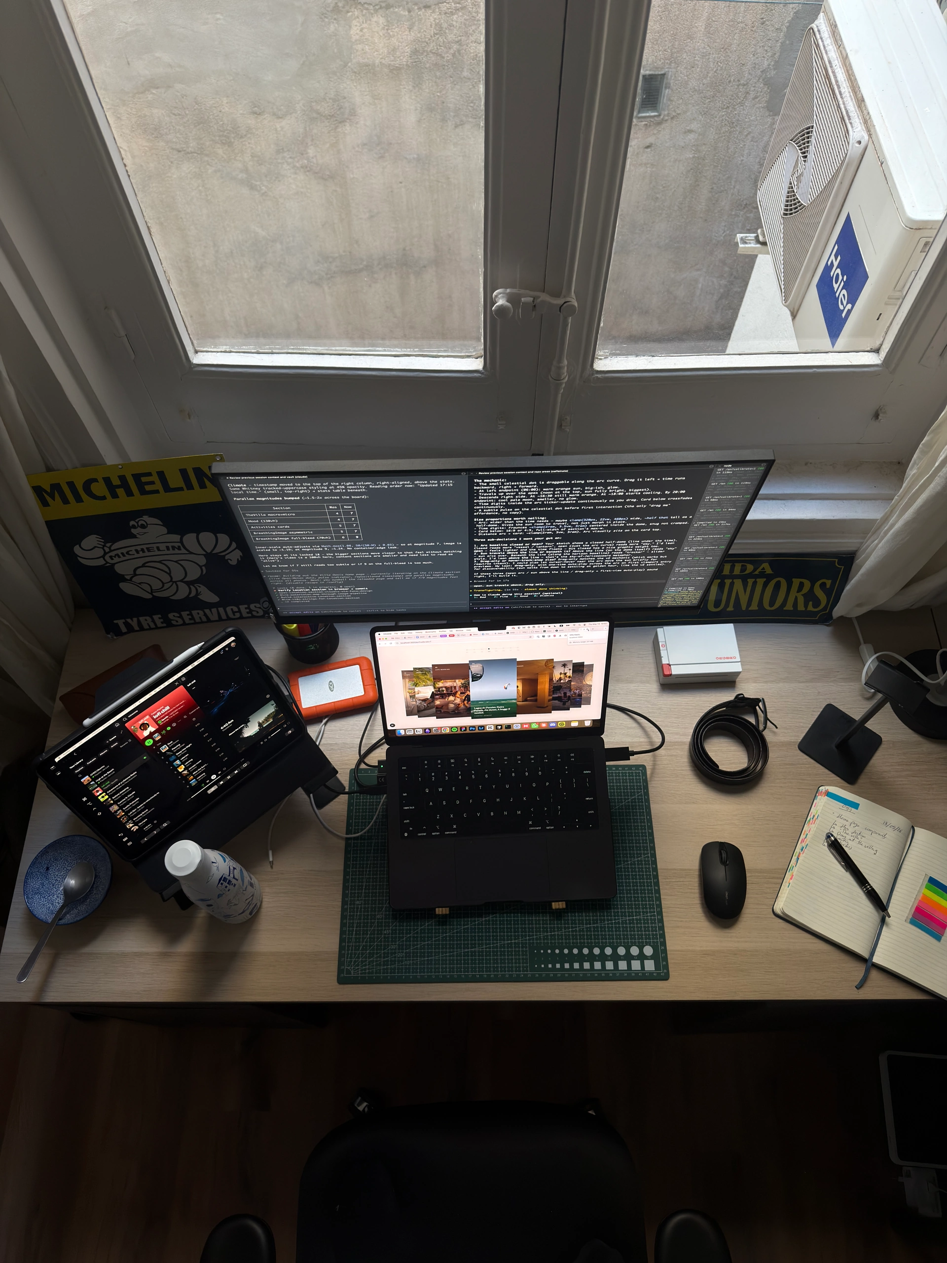 The Faca Studio desk from above: laptop, ultrawide monitor and notebook by the window